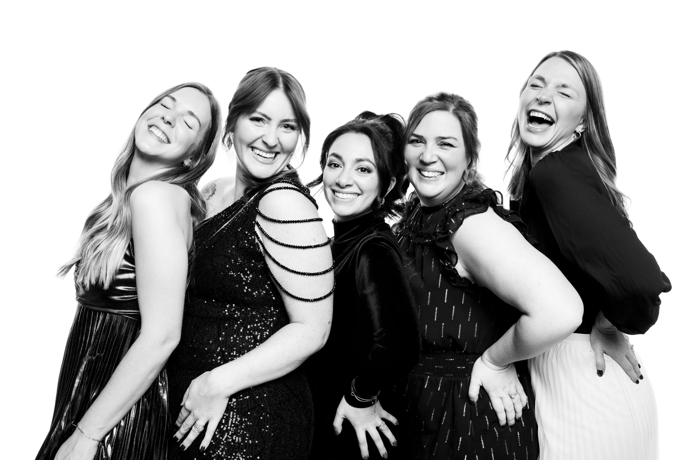Five friends in evening dresses laughing together in front of the white backdrop